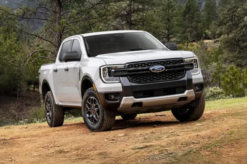 White Ford Ranger pickup truck parked on a dirt trail surrounded by trees and hills.