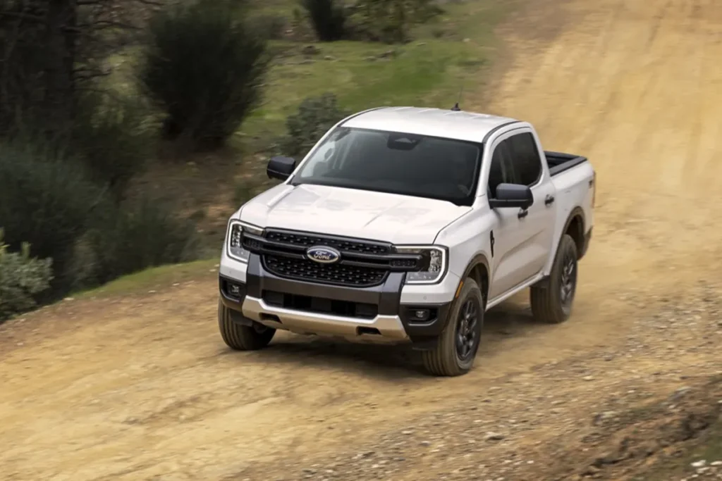 White Ford Ranger pickup truck driving on a dirt road in a rural landscape.