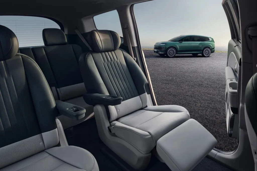 Second-row reclining captain’s chairs inside the Hyundai Ioniq 9 with leg rests extended and a view of the electric SUV parked outside.
