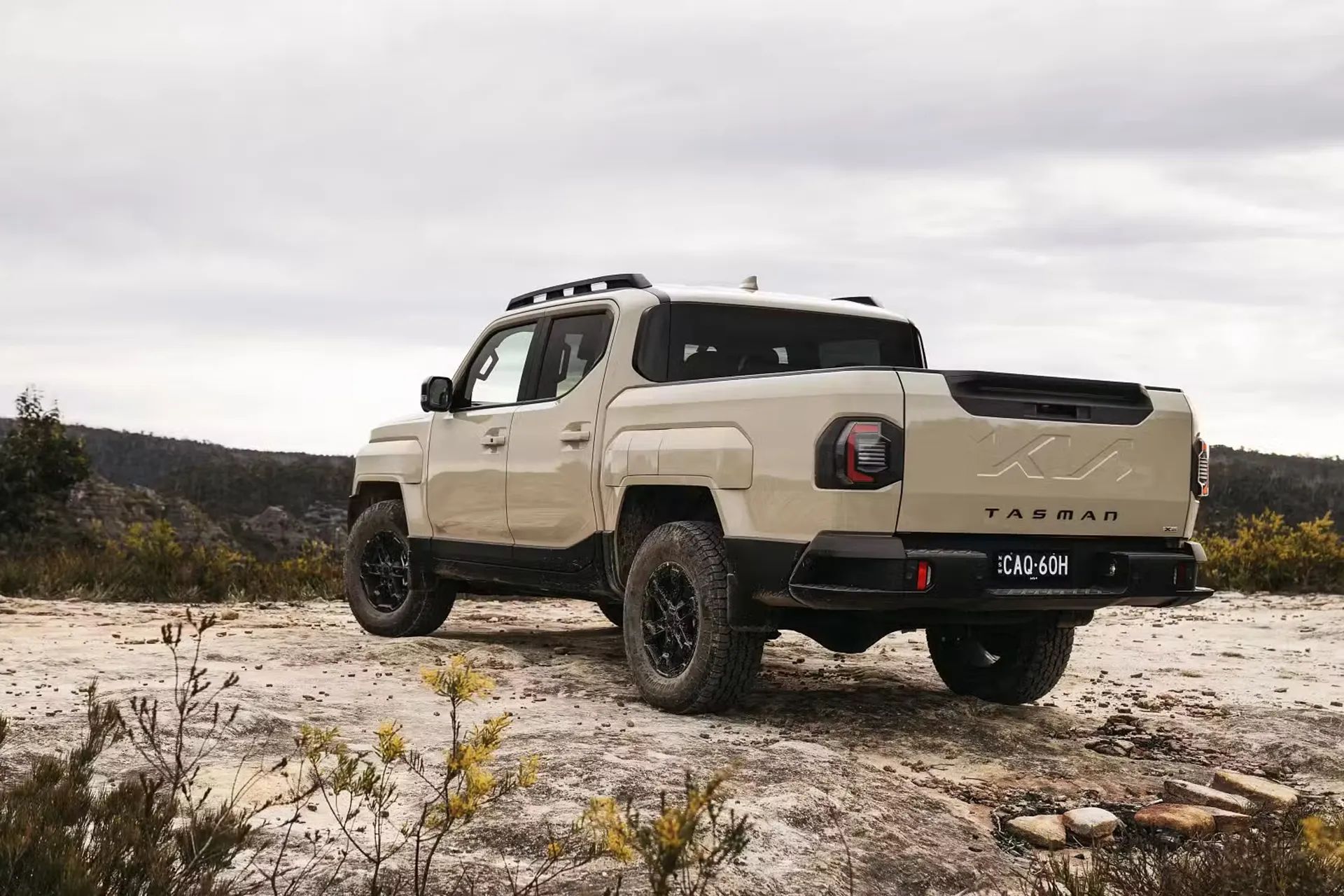 Rear three-quarter view of the 2026 Kia Tasman ute parked in rugged Australian bushland.