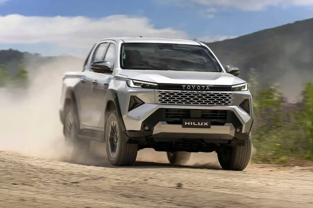 Silver Toyota Hilux pickup truck driving fast on a dusty off-road trail.