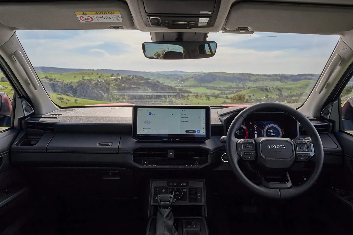 Interior of a Toyota Hilux with steering wheel, digital instrument cluster, and central infotainment screen.