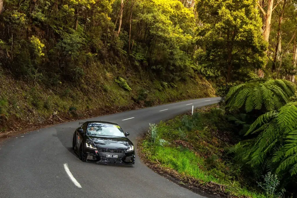 Sports car navigating tight corners on the Black Spur driving road in Victoria surrounded by dense forest