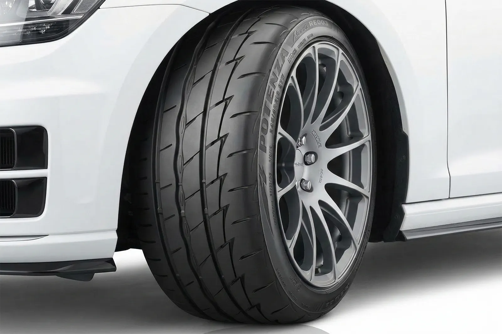Close-up of Bridgestone Potenza performance tyre on white car showing tread pattern and road contact