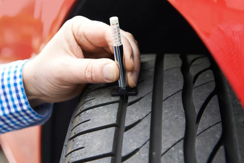 measuring tyre tread depth with a gauge to determine when car tyres need replacement