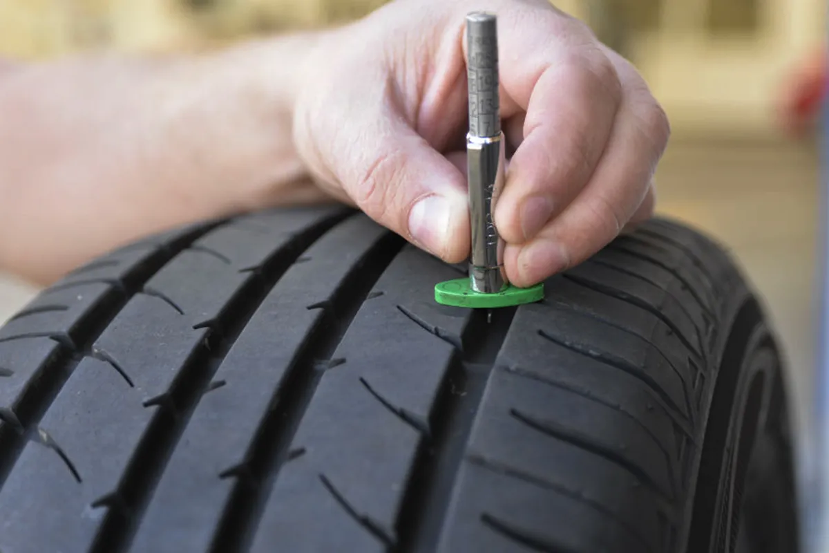 Hand using tread depth gauge to measure tyre wear and safety levels on a car tyre
