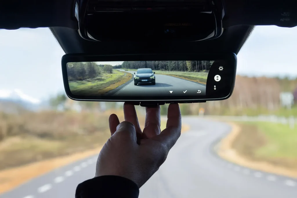 Driver adjusting a digital rearview mirror showing a clear live rear camera view on an open road