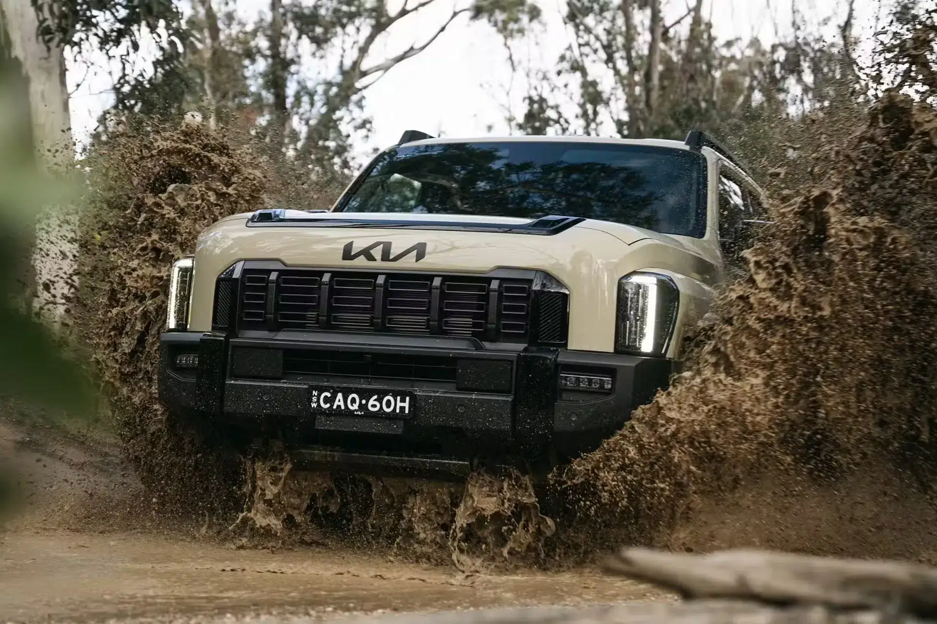 Kia Tasman 4x4 ute splashing through mud during off-road testing in the Australian bush.