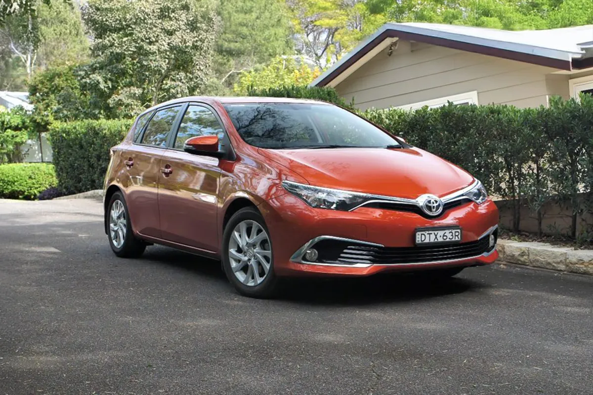 Orange Toyota Corolla hatchback parked in a residential driveway with greenery and house in background