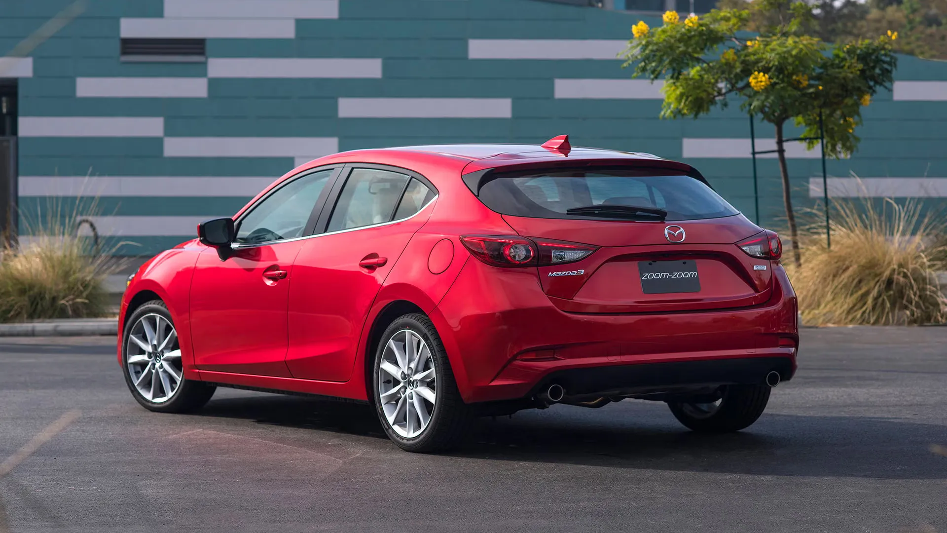 Red Mazda 3 hatchback parked outdoors, rear three-quarter view showing modern design and taillights