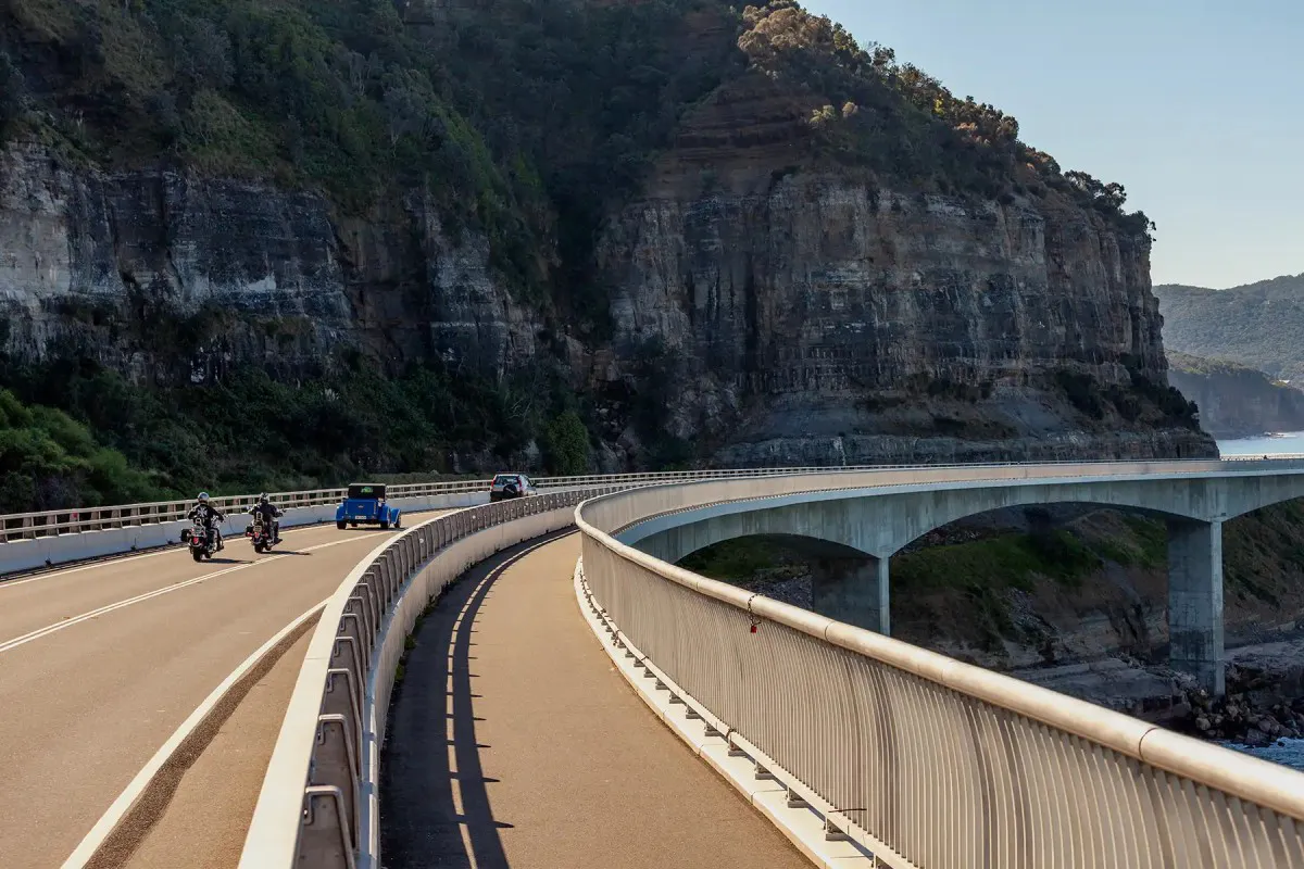 Cars and motorcycles driving along Sea Cliff Bridge with ocean views on the NSW coast