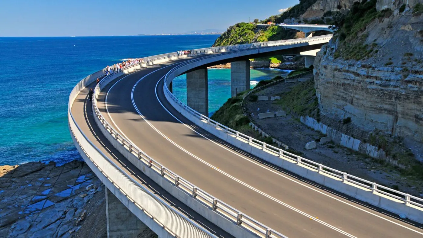 Drivers crossing Sea Cliff Bridge on the Grand Pacific Drive with ocean cliffs and coastal scenery