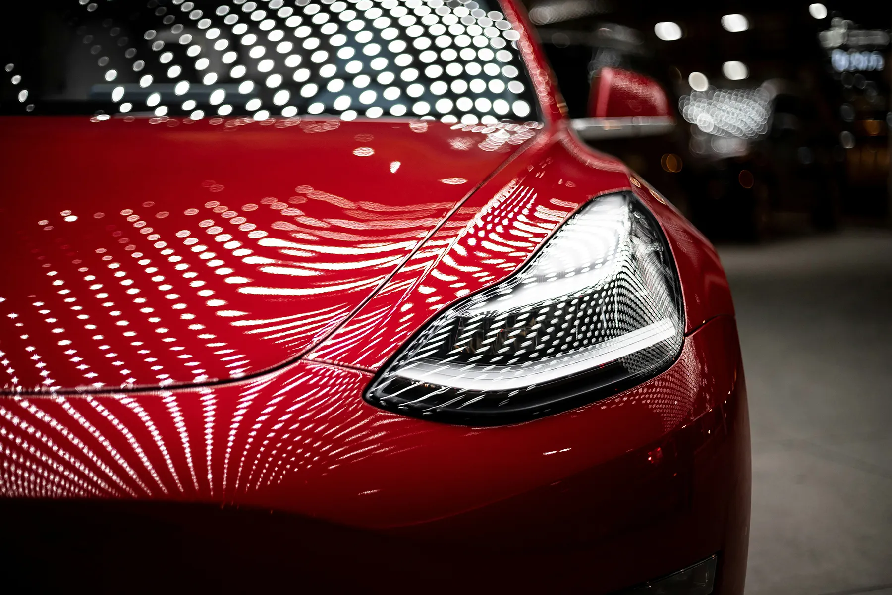 Close-up of a red Tesla's headlight reflecting studio lights, representing connected vehicle technology at the centre of Australia's 2026 car data privacy reforms
