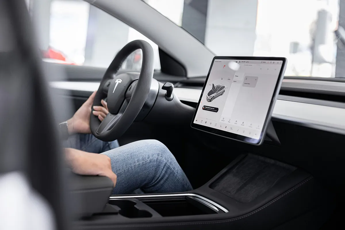 A driver sits in a Tesla holding the steering wheel beside a large touchscreen infotainment system, illustrating how modern EVs collect personal driver data in Australia