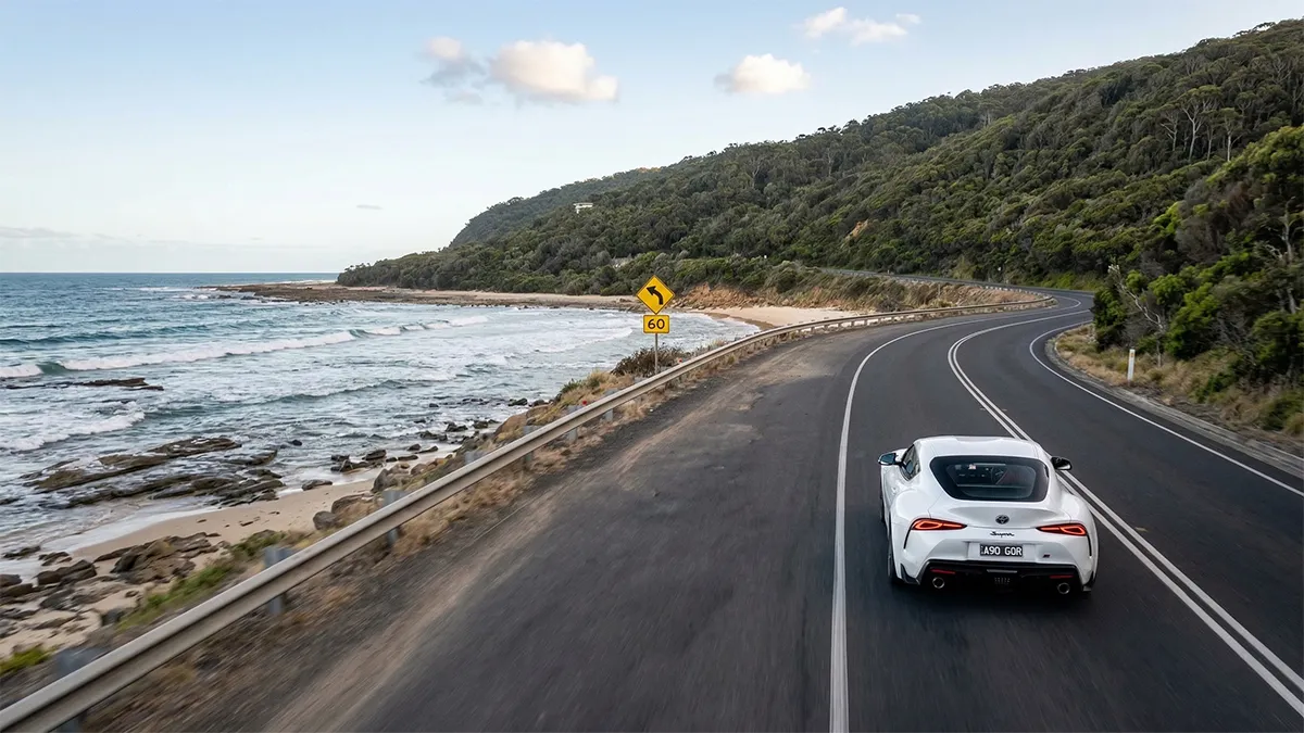TorquePress - The Great Ocean Road Drive White Toyota Supra driving on a winding coastal road at the Great Ocean Road, Victoria, Australia.