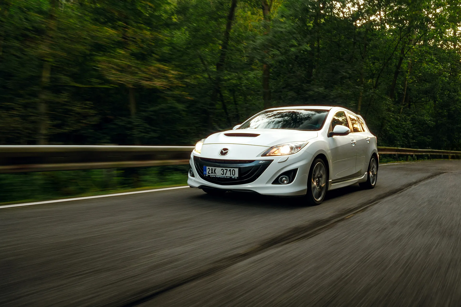 White Mazda 3 driving on a winding road through a forest with motion blur