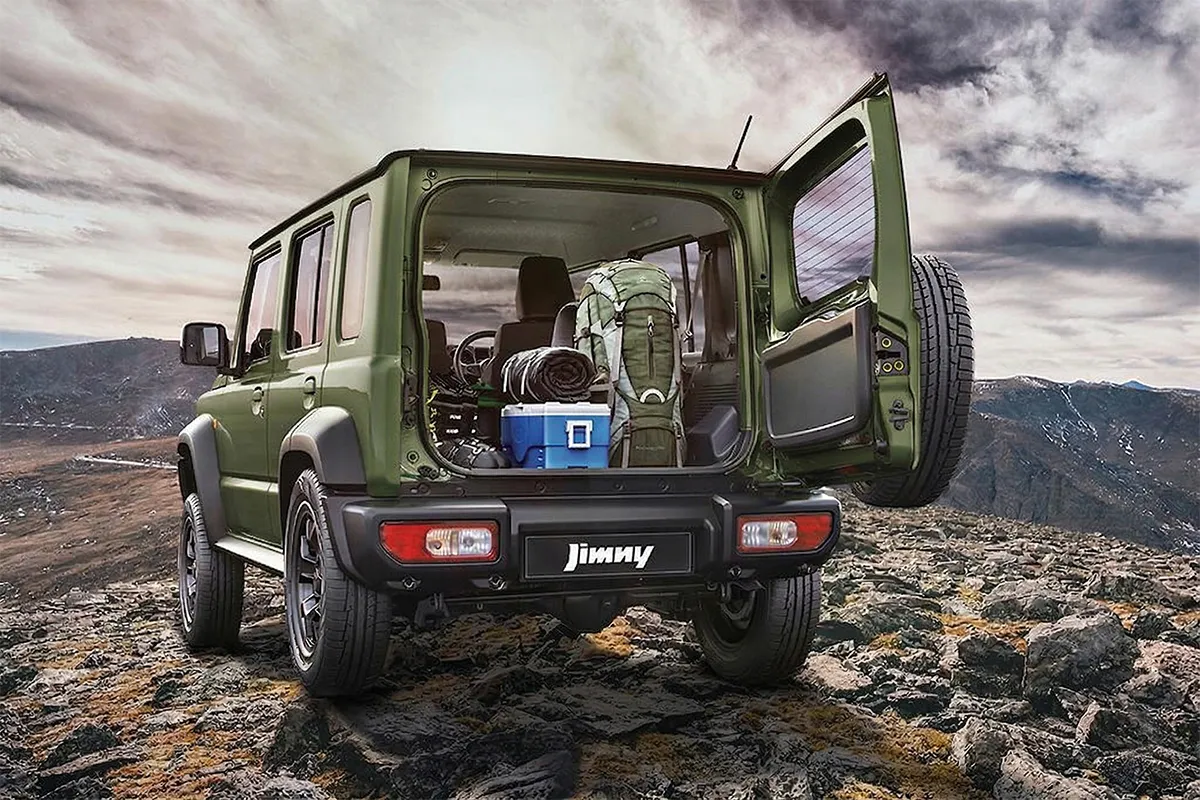 Rear view of the 2026 Suzuki Jimny with split tailgate open, loaded with a backpack, sleeping roll, and cooler on a rocky mountain summit