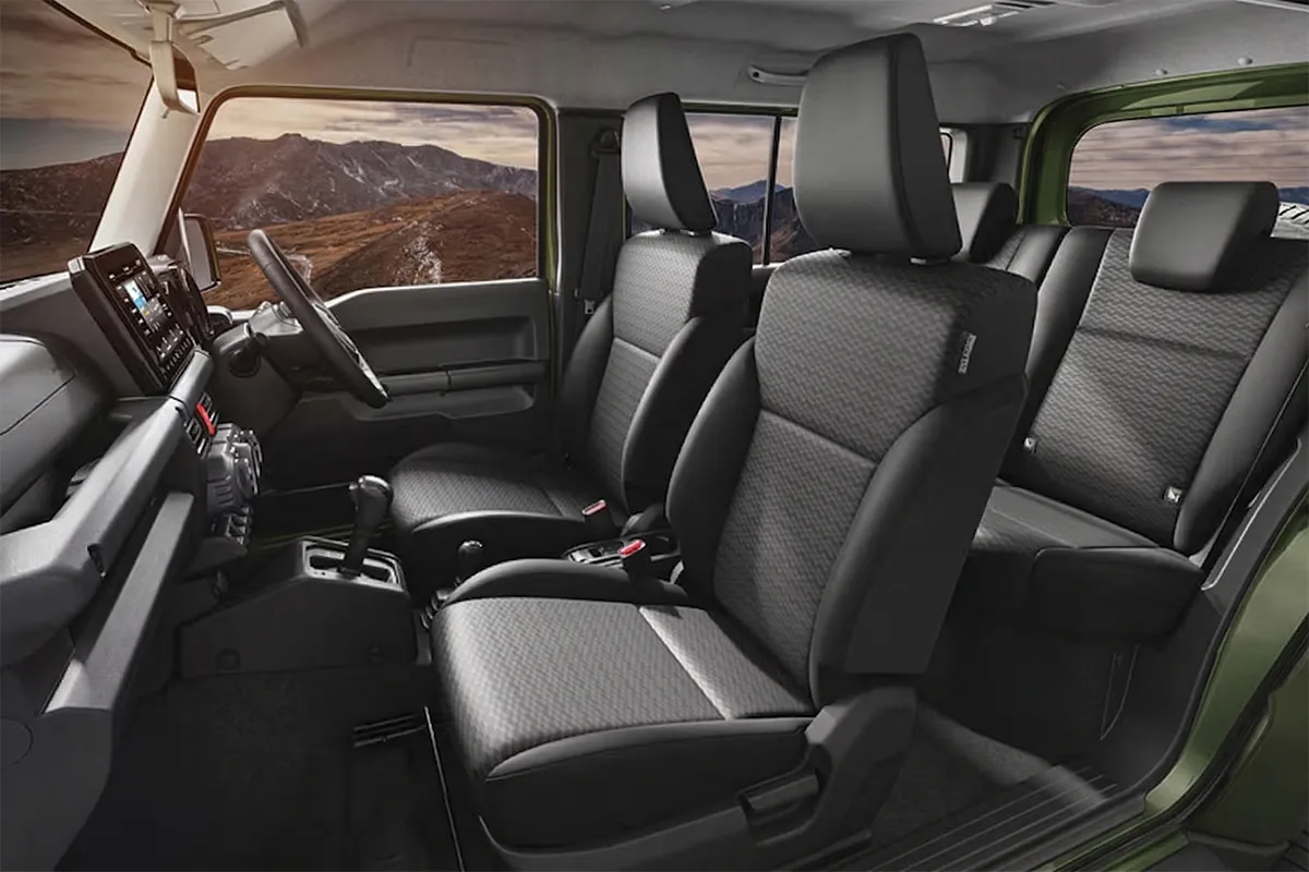 Interior of the 2026 Suzuki Jimny showing black fabric front and rear seats, gear shifter, and touchscreen infotainment system with mountain views through the window