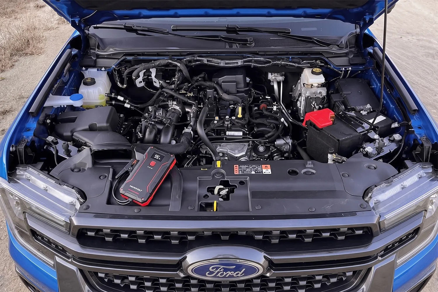 MicroVolt jump starter pack sitting on the engine bay of a blue 2026 Ford Ranger, battery terminals visible, bonnet open