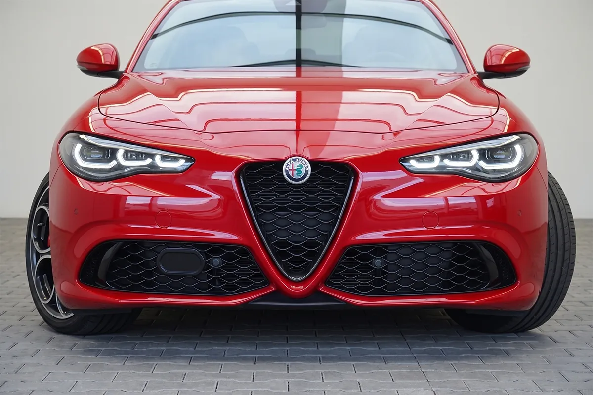 Front-on view of a red 2026 Alfa Romeo Giulia Veloce showing the signature Scudetto grille, Alfa Romeo badge, and LED Trilobe headlights