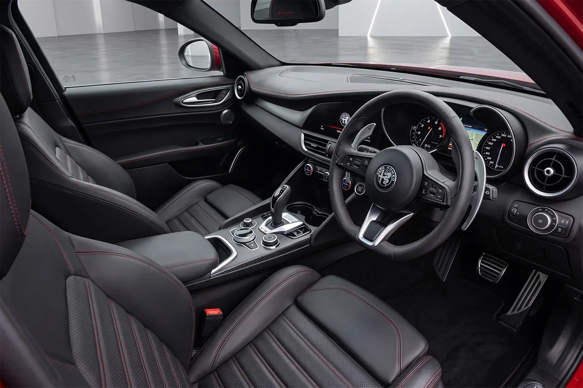 Interior of the 2026 Alfa Romeo Giulia Veloce showing the leather-wrapped steering wheel, large aluminium column-mounted paddle shifters, and DNA drive mode selector