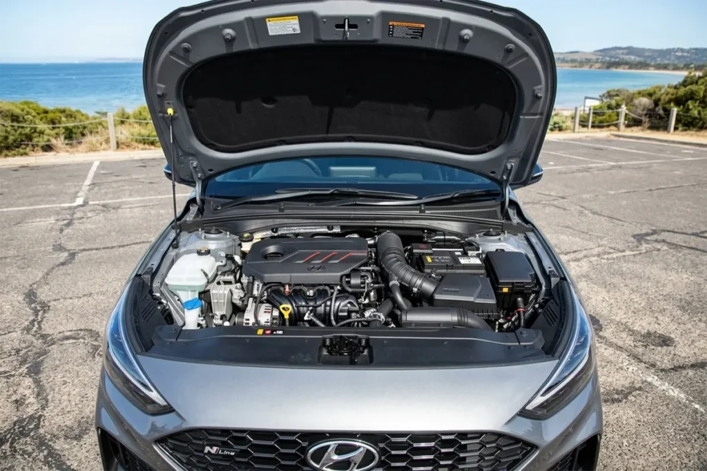Engine bay of a 2026 Hyundai i30 N Line showing the 1.5-litre turbocharged mild-hybrid four-cylinder, photographed at an Australian coastal car park