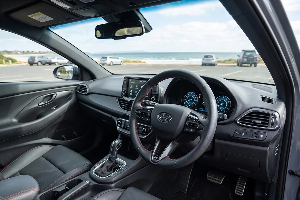 Driver-side interior of the 2026 Hyundai i30 N Line showing the digital instrument cluster, flat-bottom steering wheel and red contrast stitching