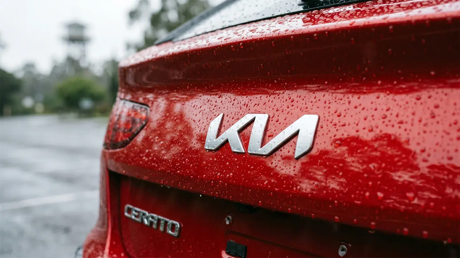 Close-up of the chrome KIA emblem and Cerato badge on the wet rear tailgate of a red 2026 Cerato GT hatchback