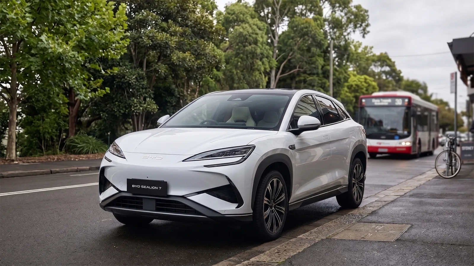White BYD Sealion 7 electric SUV parked on a Sydney street with a Transport NSW bus passing behind, the model that outsold the Tesla Model Y to lead Australian EV sales in April 2026