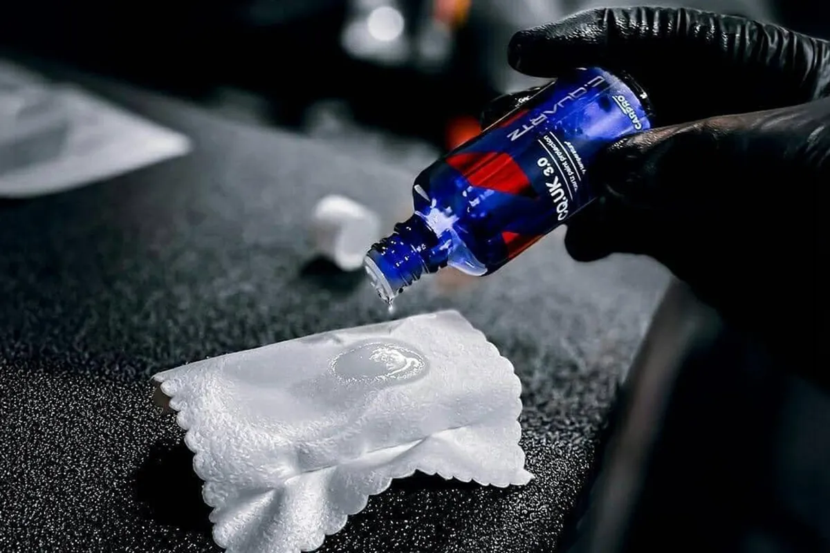 Gloved hand dispensing CarPro CQuartz UK 3.0 ceramic coating onto a white suede applicator block ready for paint application