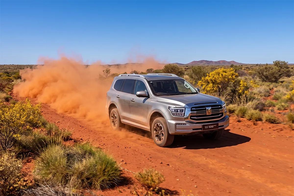 GWM Tank 500 PHEV driving on a red dirt outback road trailing a heavy dust cloud