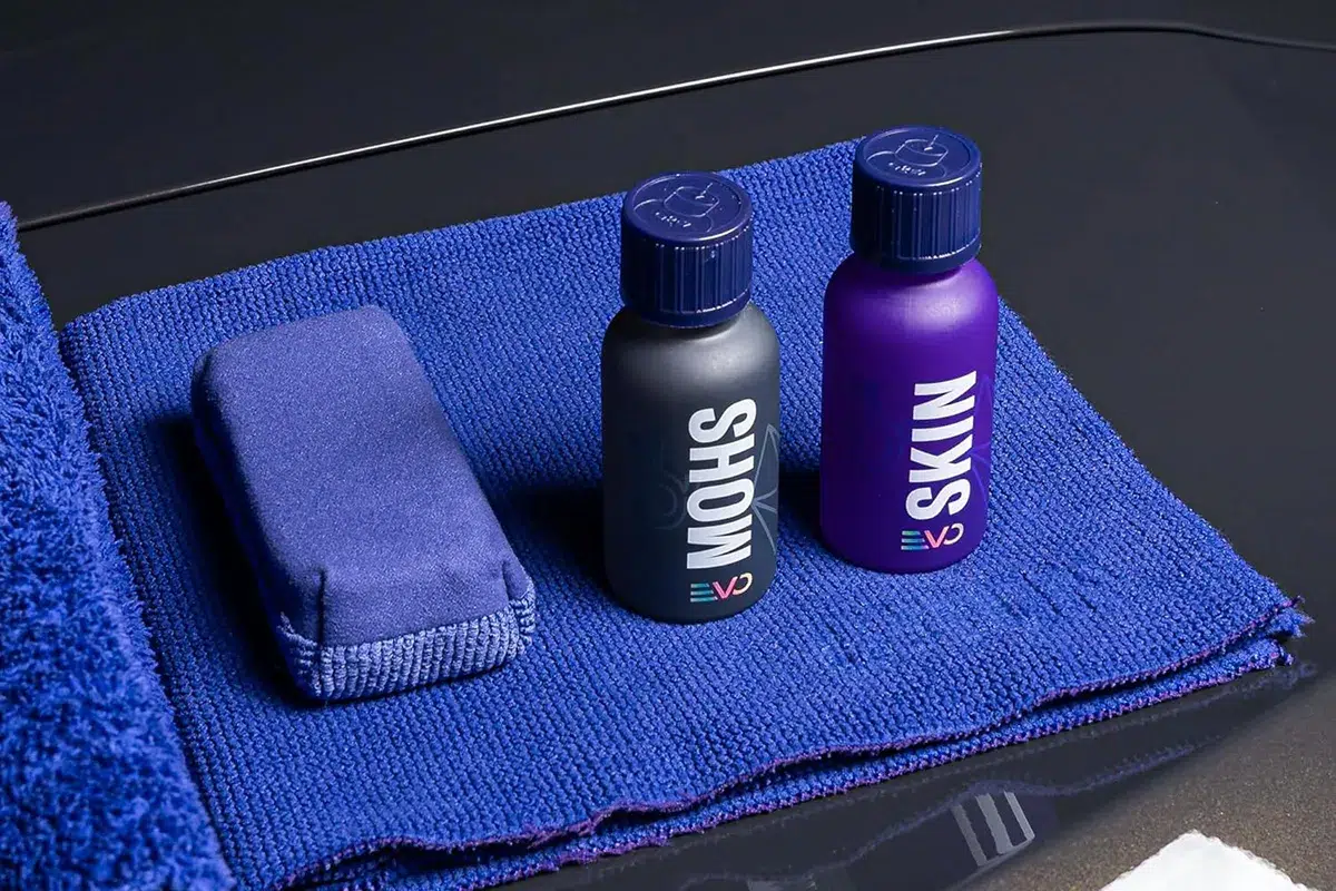 Gyeon Q2 Syncro EVO Light kit showing Mohs EVO base coat and Skin EVO topcoat bottles with applicator pad on a blue microfibre towel