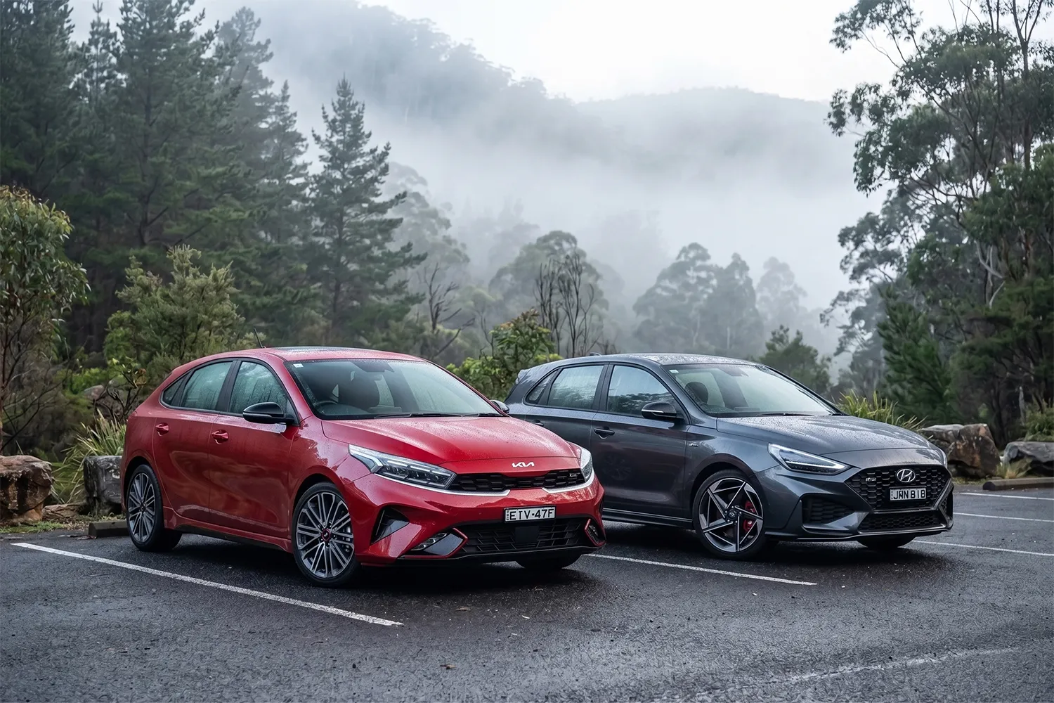 kia-cerato-gt-hyundai-i30-n-line-comparison-2026 Red 2026 Kia Cerato GT and grey Hyundai i30 N Line hatchbacks parked side by side at a misty Australian mountain lookout