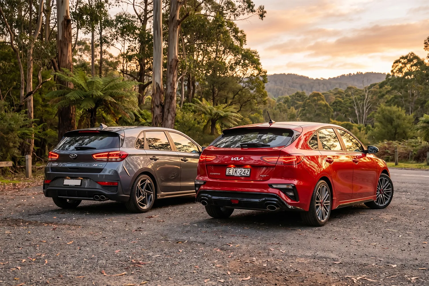 Rear view of a red 2026 Kia Cerato GT and grey Hyundai i30 N Line parked at an Australian forest lookout at sunset