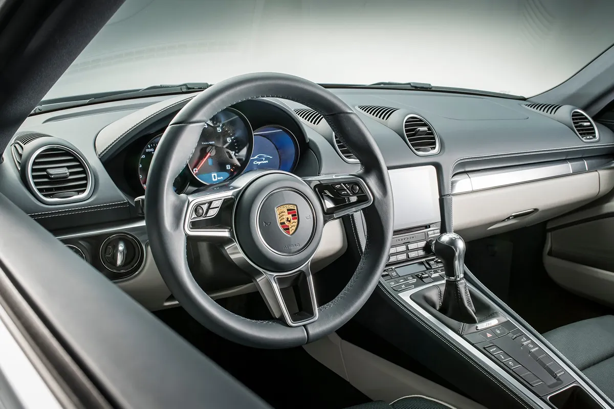 Interior dashboard and steering wheel view of the 2026 Porsche 718 Cayman showing physical button layout