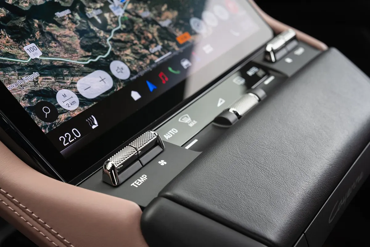 porsche-cayenne-electric-physical-toggle-switches-climate-controls Close-up of the new Porsche Cayenne Electric centre console showing knurled metal toggle switches for temperature and climate controls alongside the touchscreen