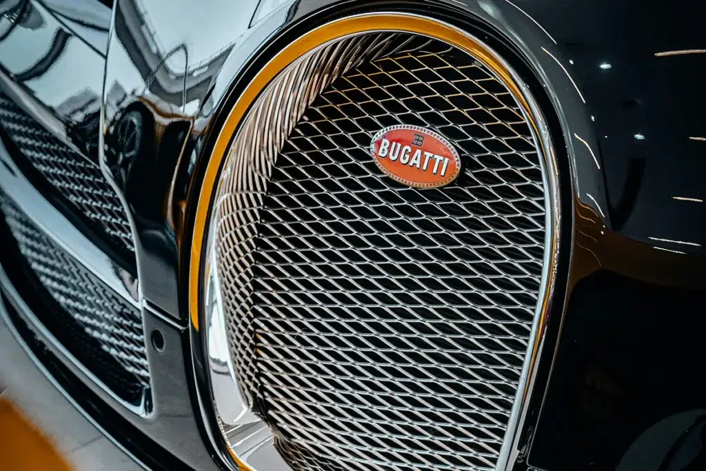 Close-up of the Bugatti horseshoe grille with gold trim surround and red oval Bugatti badge, polished black bodywork reflecting showroom lighting