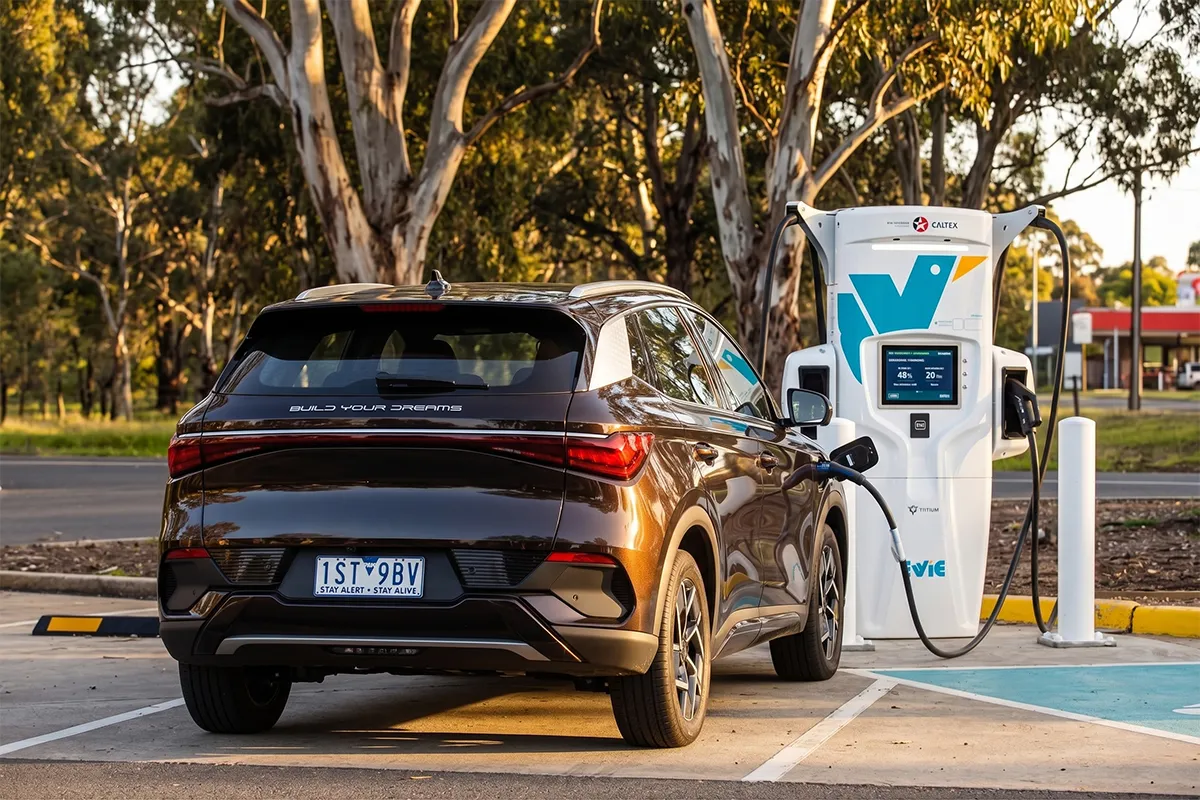 BYD Atto 3 plugged into an EVie DC fast charger at golden hour, showing the early Build Your Dreams tailgate badge