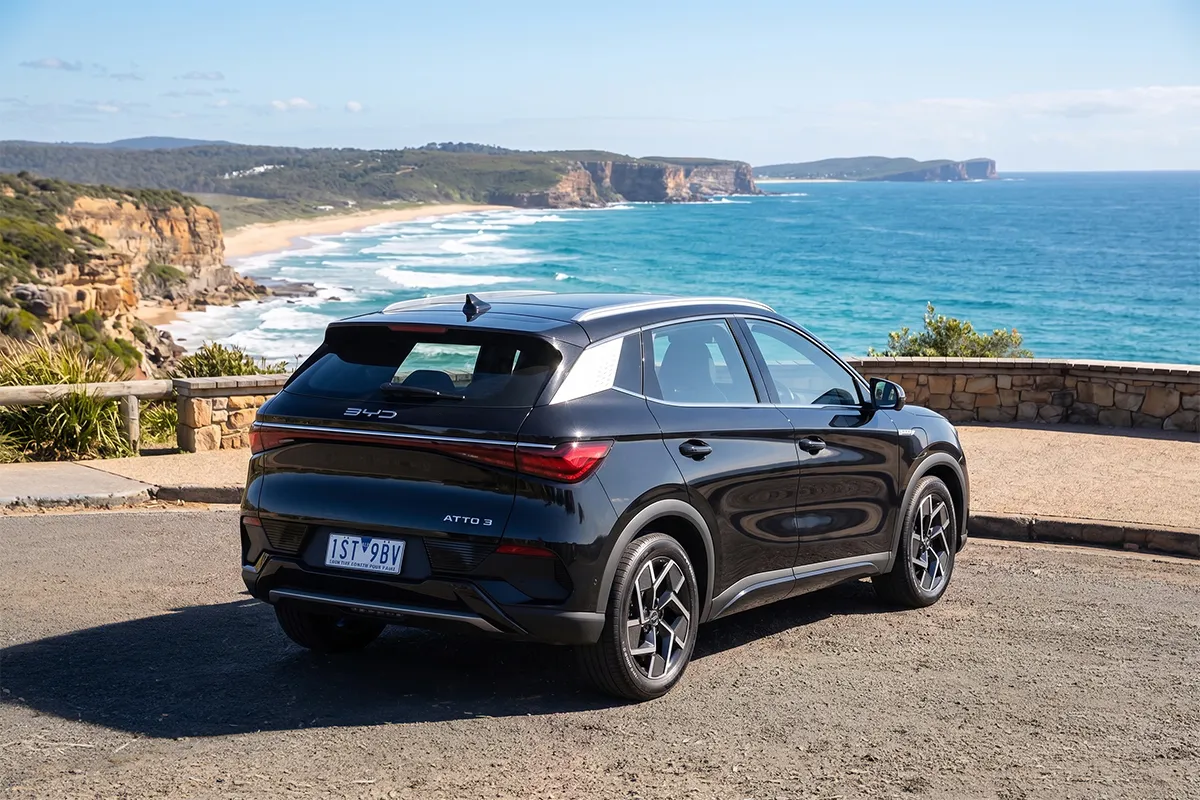 Black BYD Atto 3 parked rear-three-quarter at a clifftop coastal lookout overlooking the ocean, with the Atto 3 tailgate badge visible