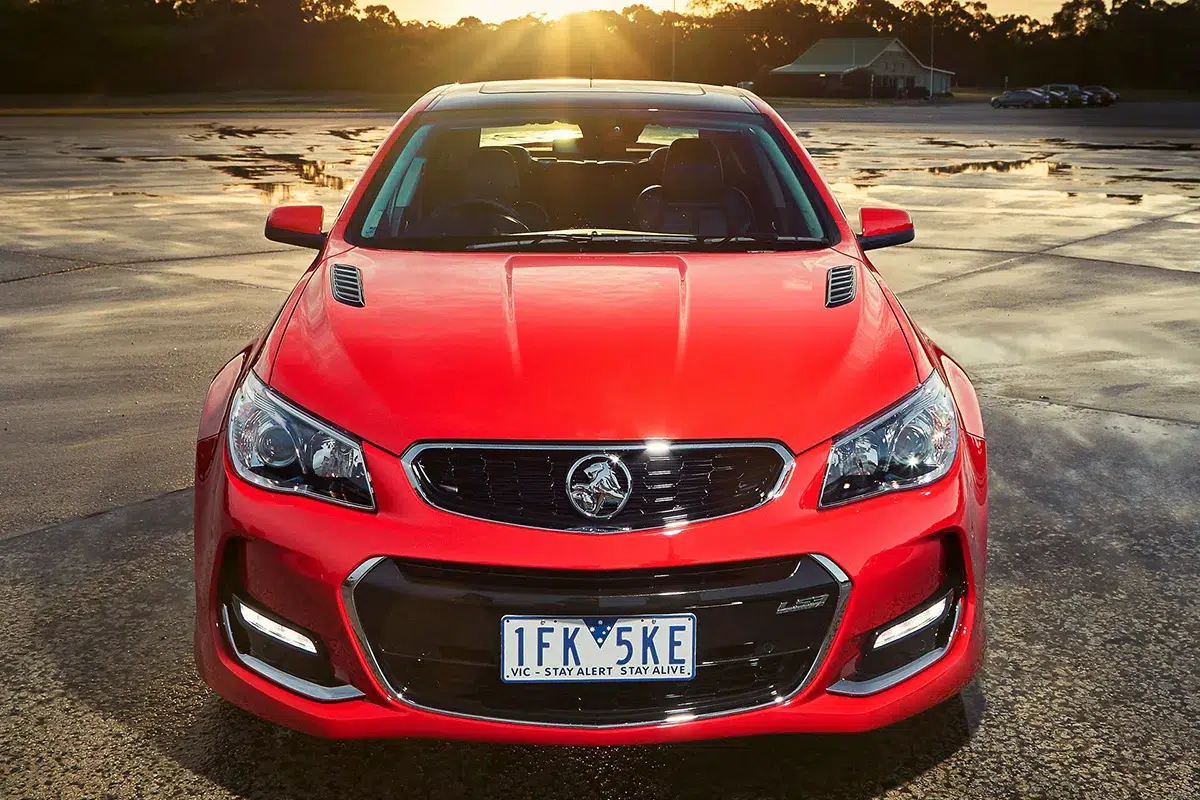 Red Holden VF Series II Commodore SS facing the camera at sunset on wet tarmac with dramatic golden sky