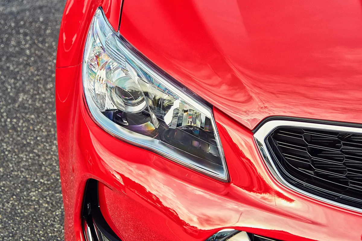 Close-up of the projector headlight on a red Holden VF Series II Commodore SS showing HID lens and chrome surround