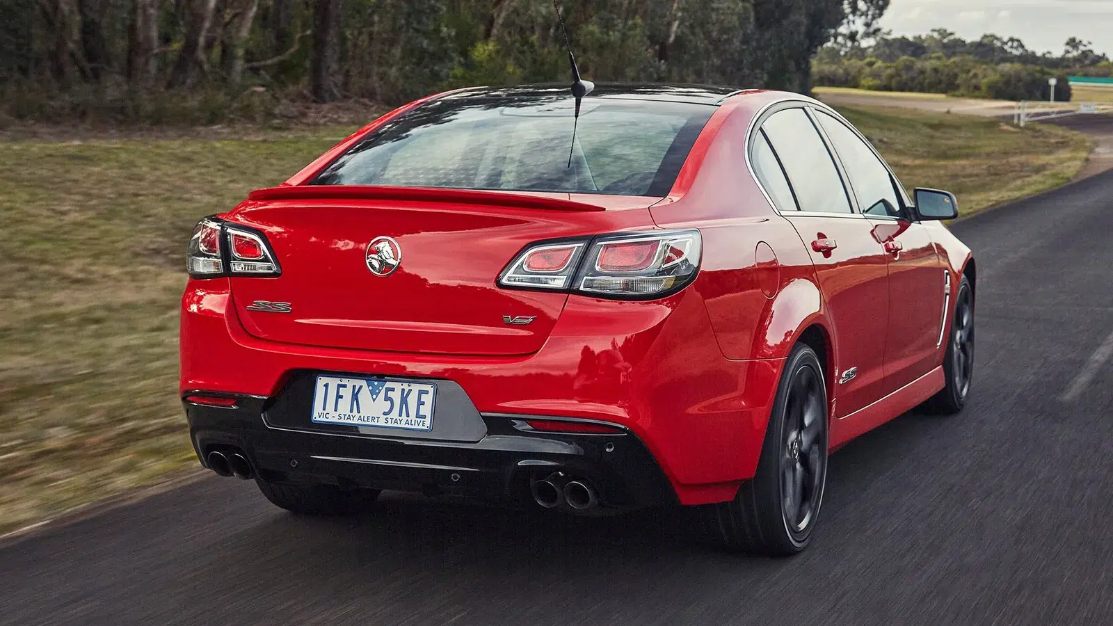 Red Holden VF Series II Commodore SS V driving on an Australian road, rear three-quarter view with Victorian plates