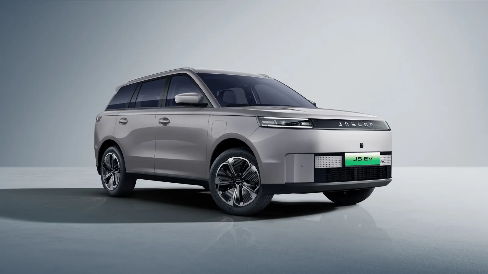 Silver Jaecoo J5 EV in a studio setting, front three-quarter view showing the closed-off EV grille and green plate