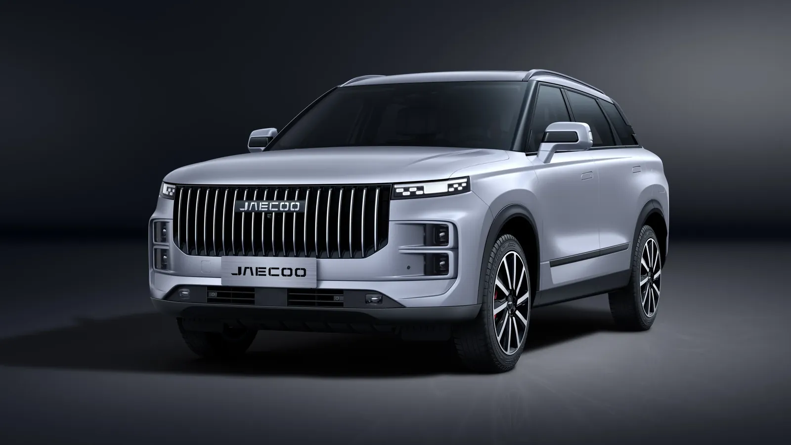 Silver Jaecoo J8 in a studio setting showing the tall vertical-slat grille and large JAECOO badge, front three-quarter view