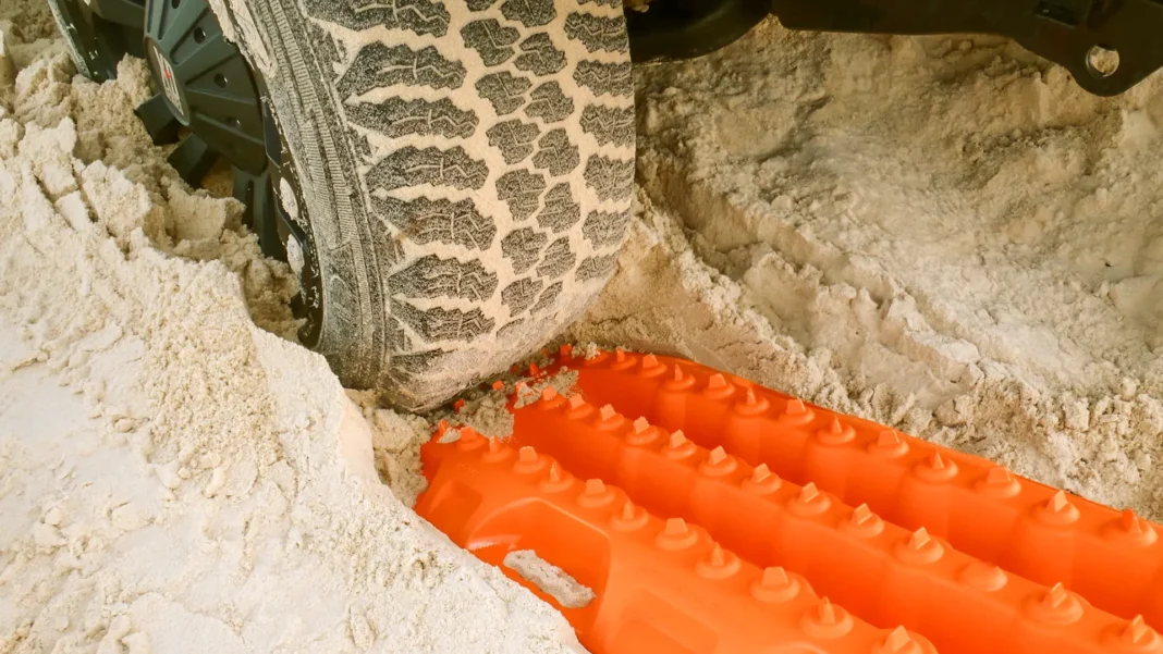 maxtrax-recovery-board-under-tyre-sand Orange Maxtrax recovery board positioned under a bogged 4WD tyre in deep white sand