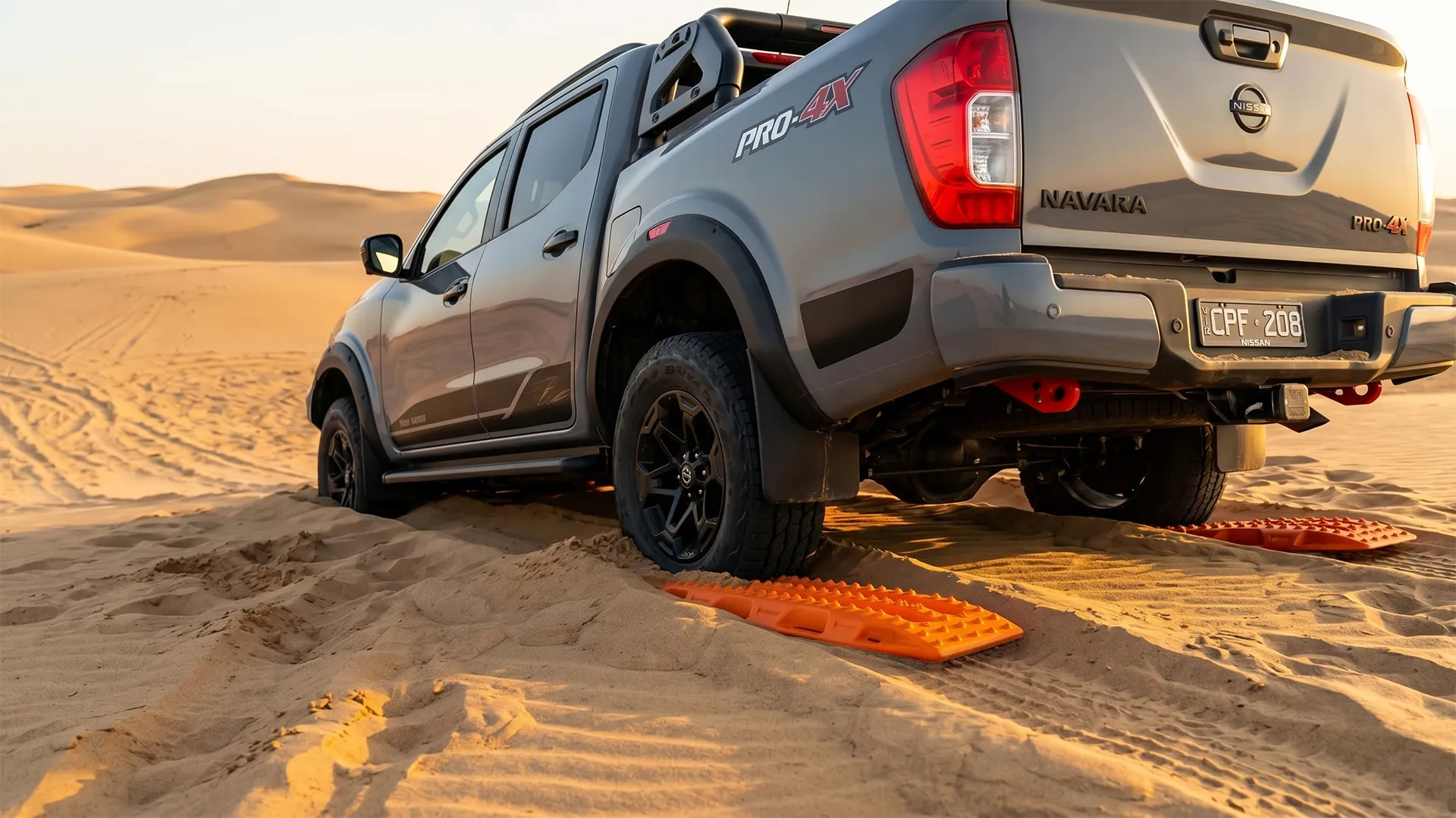 Orange recovery boards under the rear tyres of a Nissan Navara Pro-4X bogged in desert sand