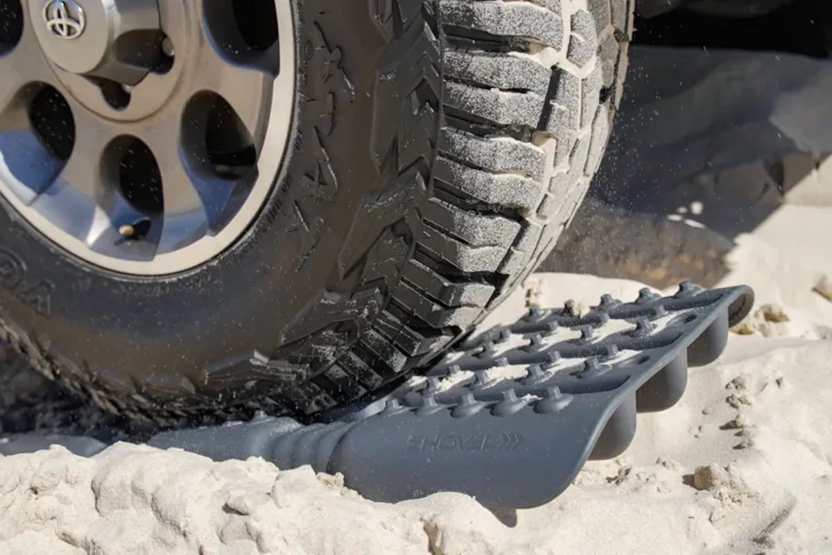 Grey recovery board being slid under a bogged 4WD tyre in beach sand