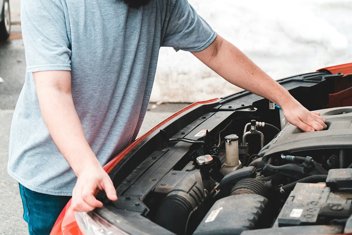 A person lifting the bonnet of a used red car to inspect the engine bay, illustrating the physical checks that an OBD2 scanner cannot replace
