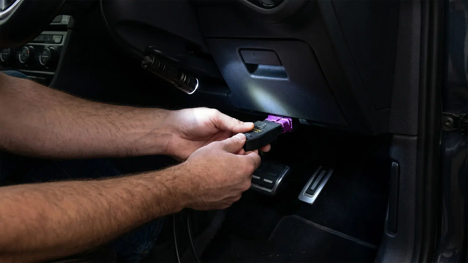 Hands plugging a VCDS HEX-V2 diagnostic cable into the OBD2 port under the dashboard of a Volkswagen