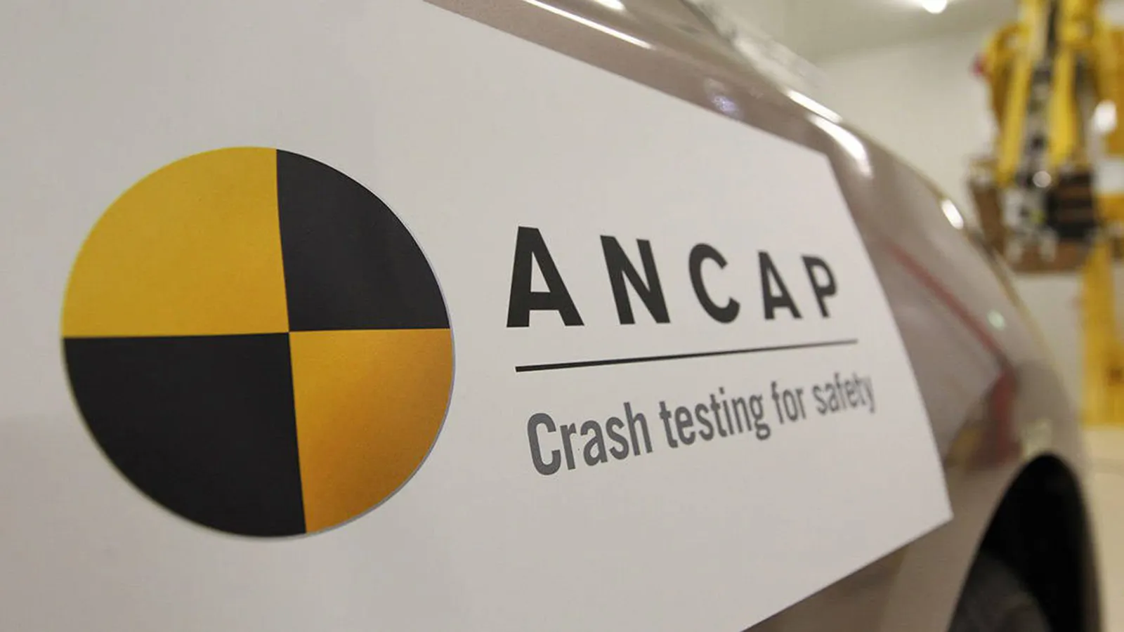 A close-up photograph of an official ANCAP safety rating sticker on the grey bodywork of a vehicle, displaying the text "ANCAP" and "Crash testing for safety".